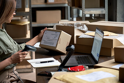 woman scanning box at desk with laptop in shipping warehouse